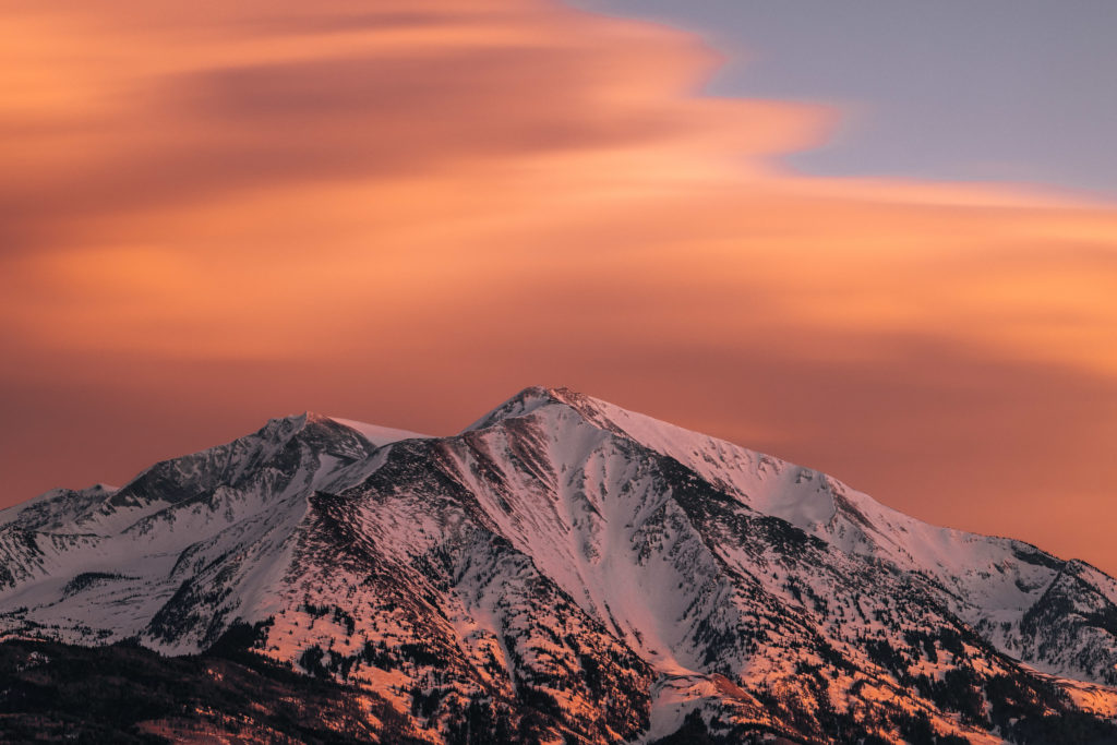 Alpenglow on the snow-covered summit of Mount Sopris beneath sweeping orange lenticular clouds